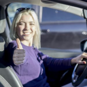 Happy woman inside a car driving in the street and gesturing thumb up